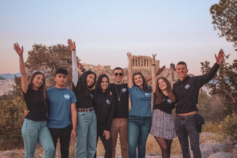 Erasmus Life Athens crew with their hands in the air in front of the Parthenon at sunset